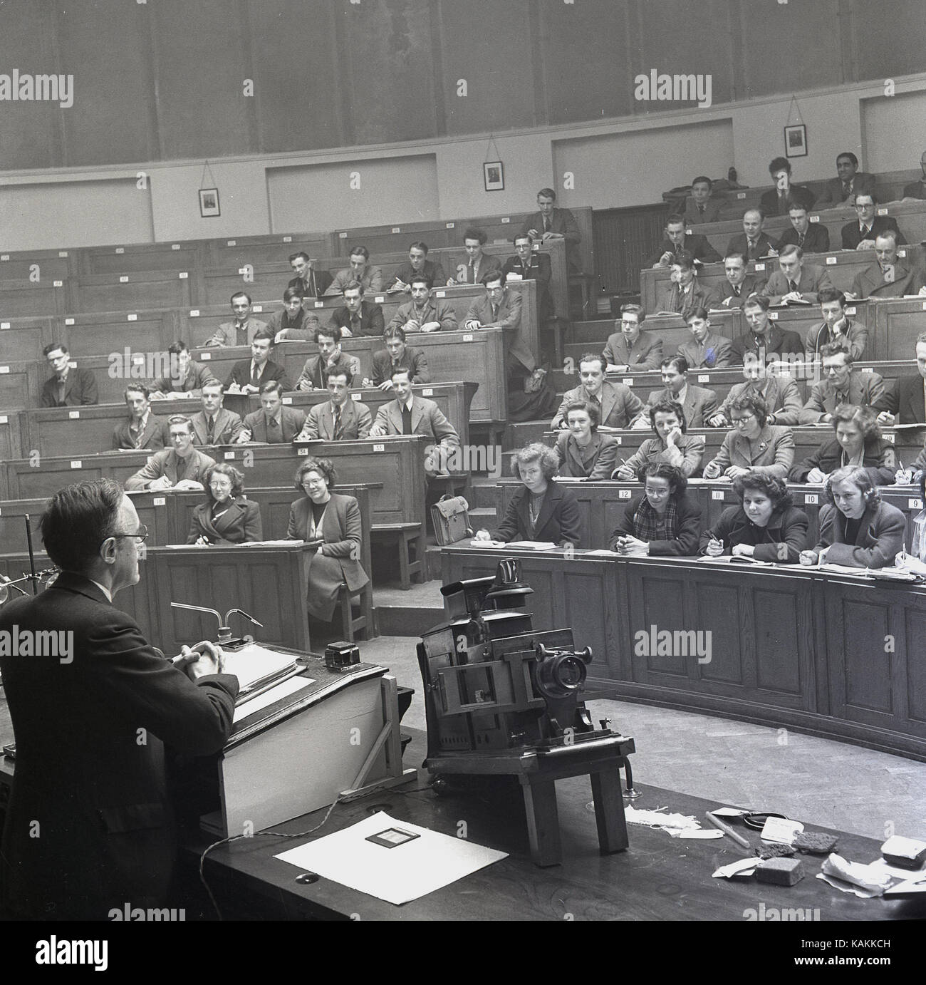 1950s, smartly dressed university students attending a class given by a male professor at the lecturn in the main chemistry lecture theatre at Leeds University, Leeds, England, UK. Stock Photo
