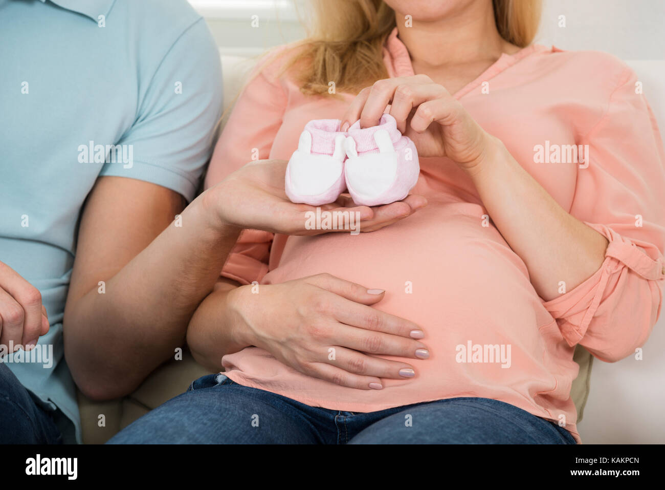 Midsection of expecting couple holding baby shoes on sofa at home Stock Photo