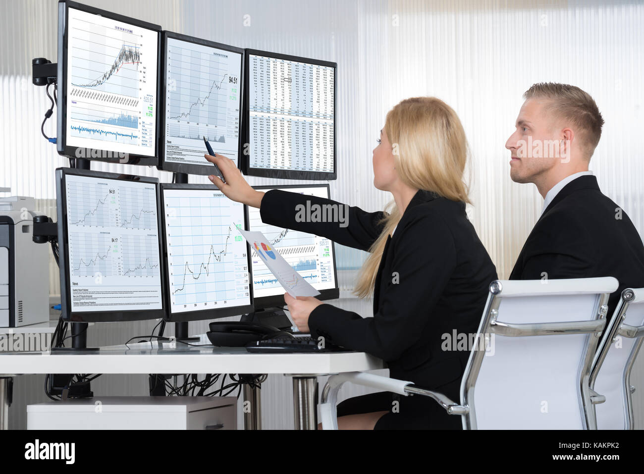 Financial workers analyzing data displayed on computer screens at desk in office Stock Photo
