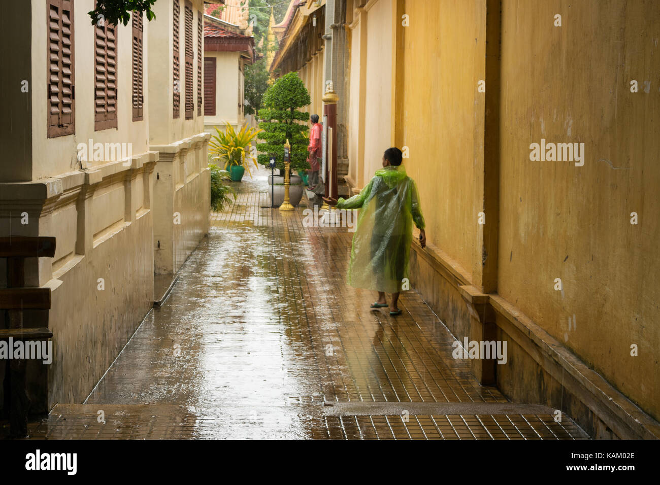 A teenager wearing a transparent green rain jacket, checking if the  the heavy monsoon rain stopped, after a heavy shower in Phnom Penh city, Cambodia Stock Photo