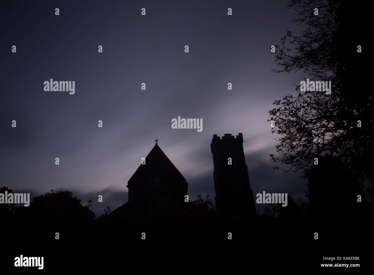 Long exposure of silhouette of a church at dawn making a scary, creepy, eerie scene with blurred clouds Stock Photo