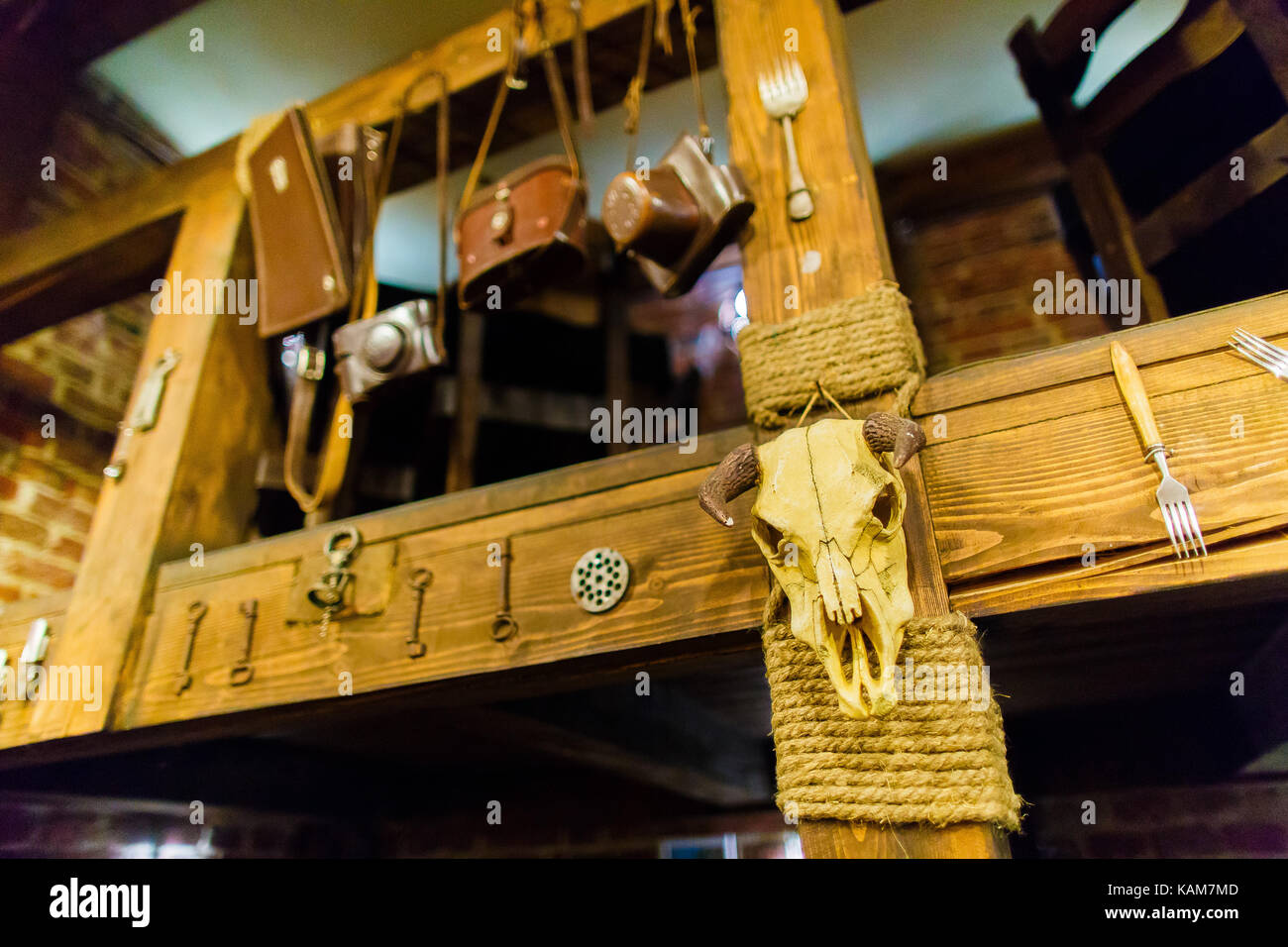The horizontal photo of the bull skull hanging on the wooden stairs decorated with keys, forks and pouches for cameras in the cafe. Stock Photo