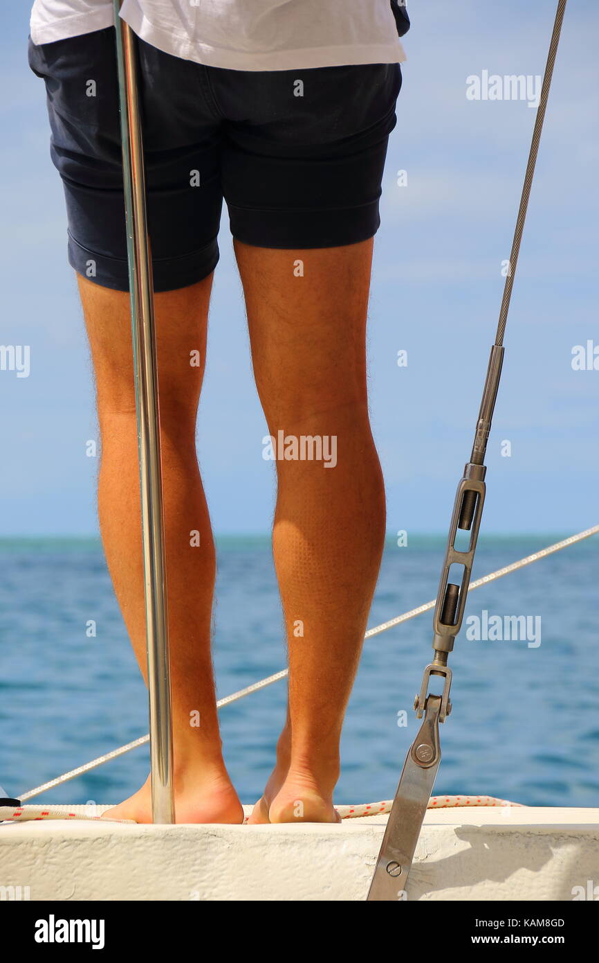 View from behind of sun tanned human legs on the deck of a yacht in portrait format with a tropical island background with copy space Stock Photo