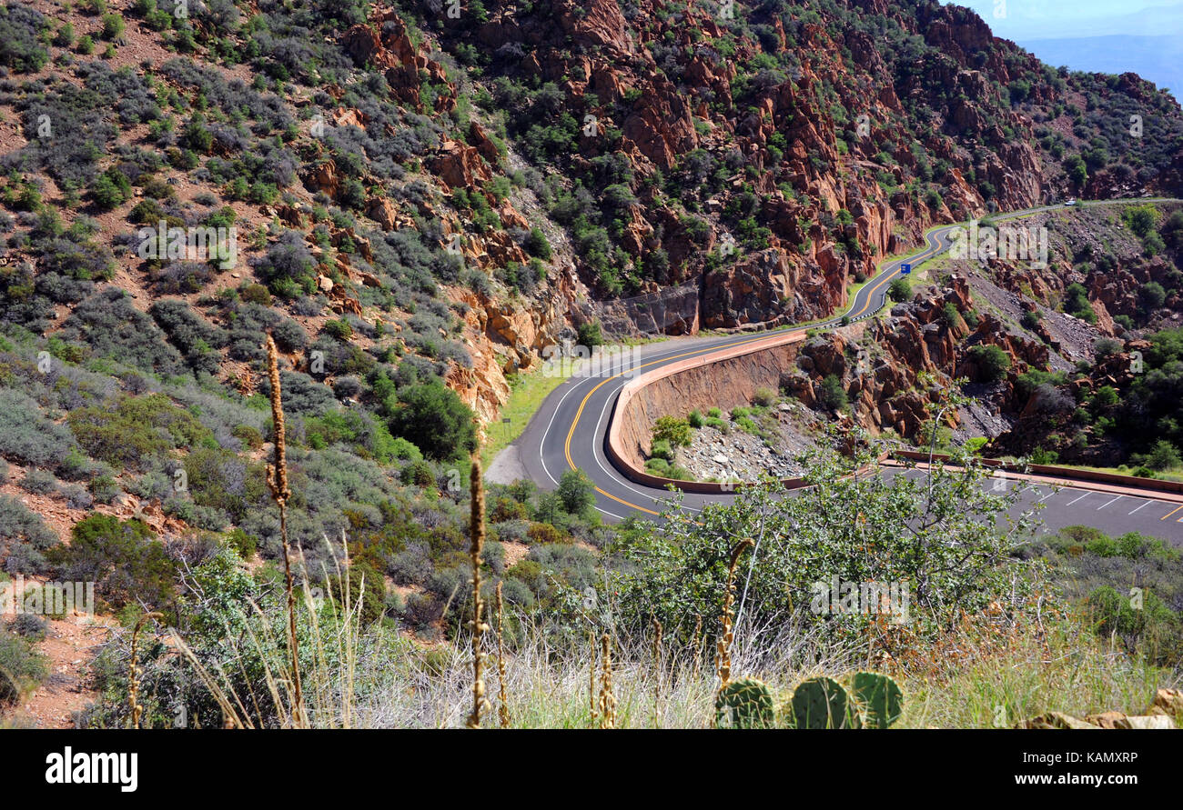 Curving mountain road winds its way to Jerome, Arizona.  Red rocky cliffs overhand highway. Stock Photo