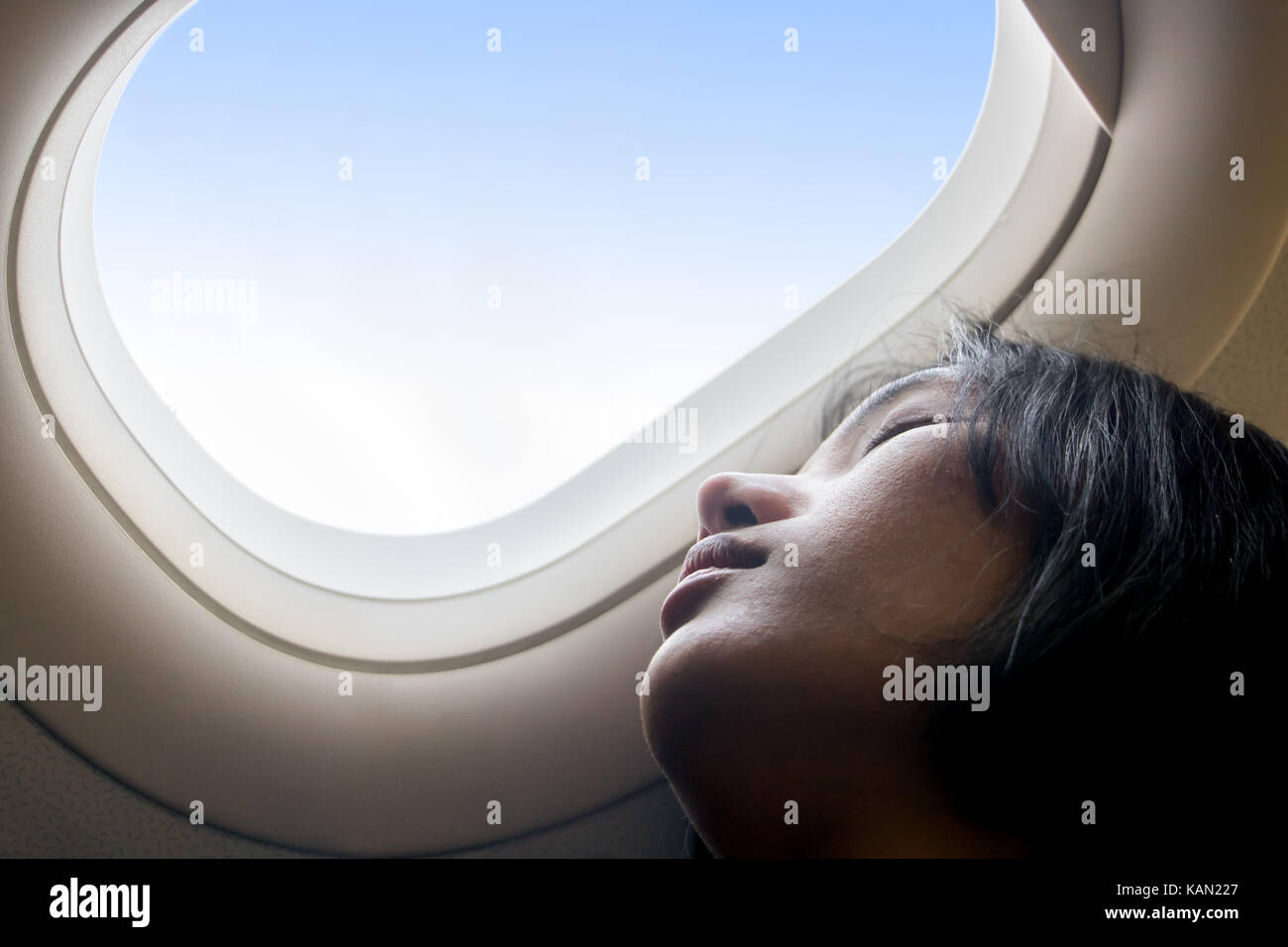 Portrait of a girl resting on an airplane. A young woman sleeping at a window of a flying plane. Dreaming in the clouds. Stock Photo