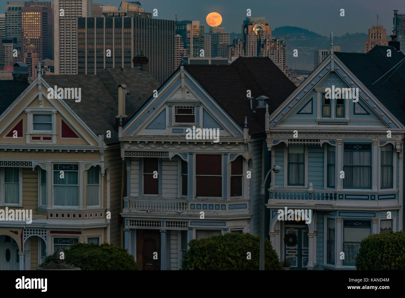 Painted Ladies Victorian houses in San Francisco, California, USA, with full moon rising behind houses and city skyline. Stock Photo