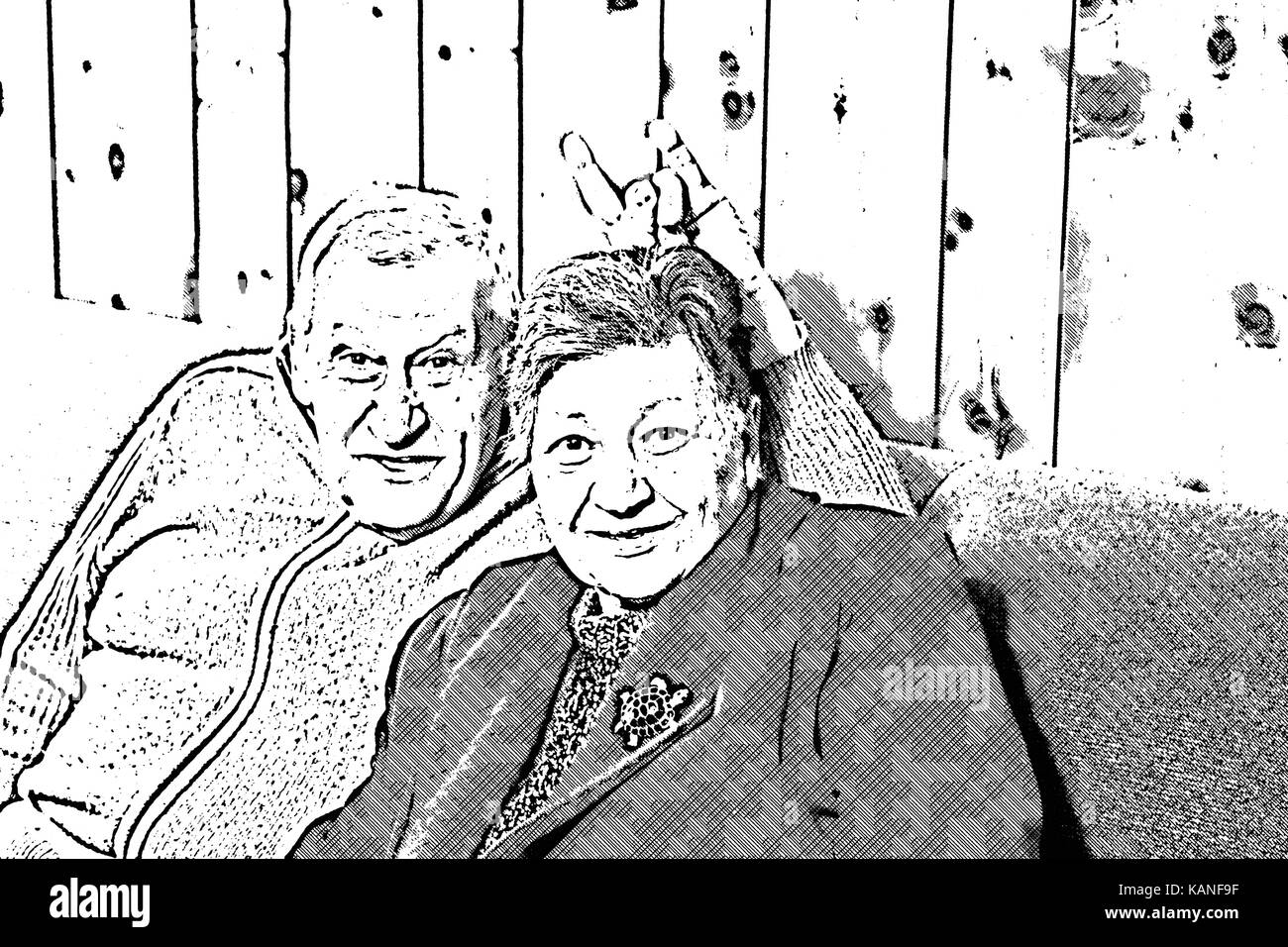elderly couple kidding while sitting on the sofa in their living room, the man make horns sign on the head of his wife Stock Photo