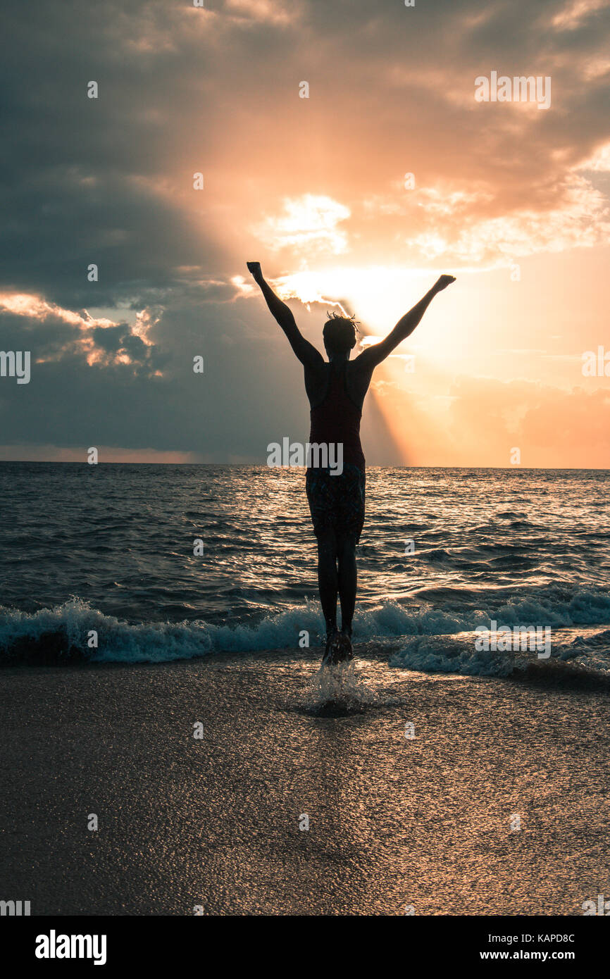 Silhouette of boy with Raised Hands and Jumping Around on the Beach at Sunset. Space available for writing quotes or any text. Stock Photo