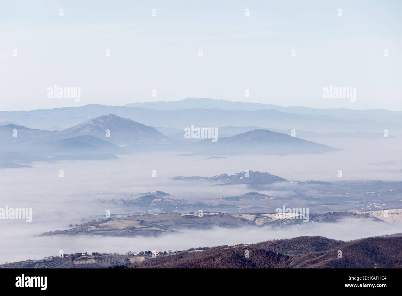 A valley filled by fog, with some hills in the foreground and other hills and mountains in the background Stock Photo