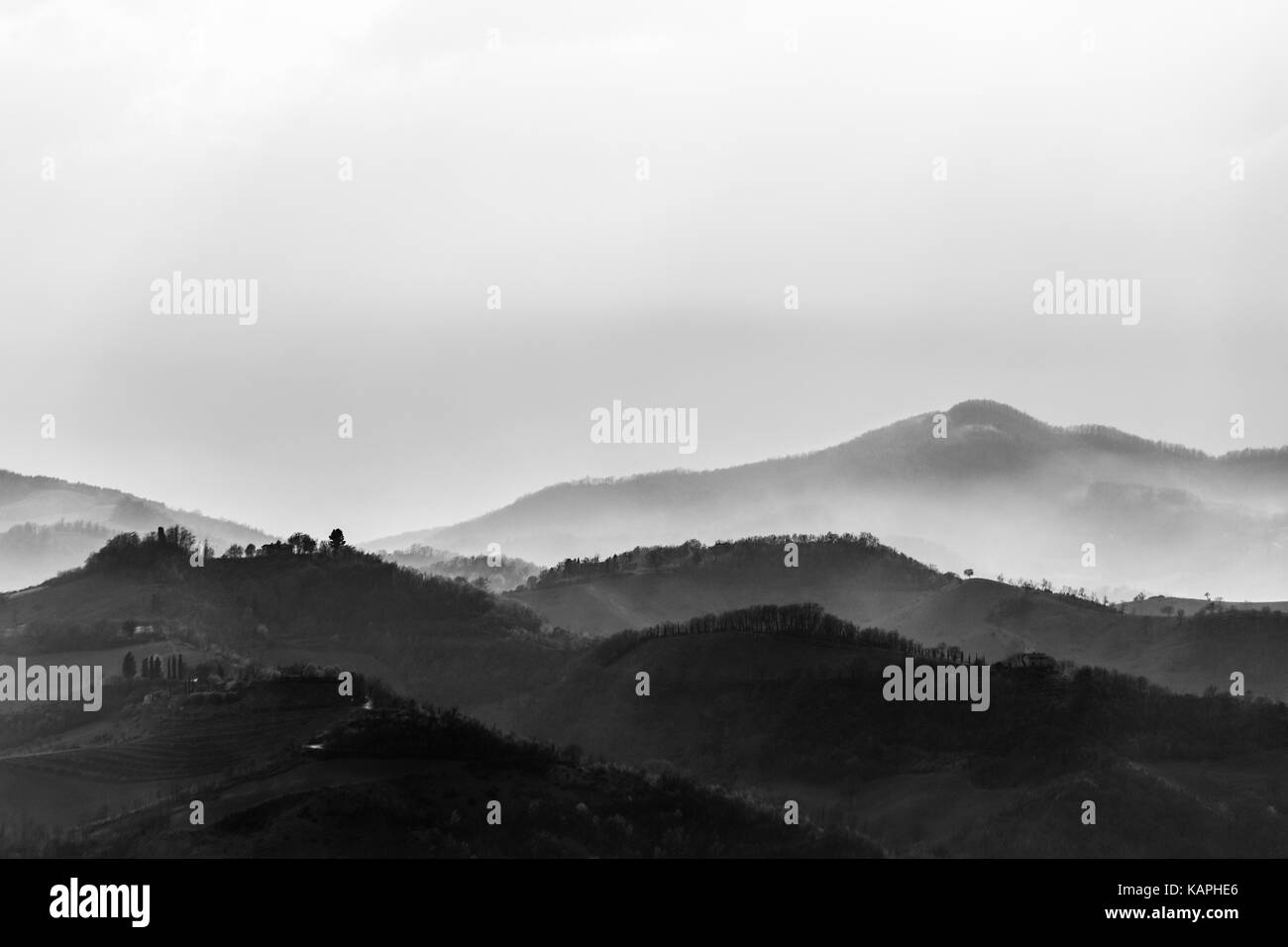 A valley filled by fog, with some hills in the foreground and other hills and mountains in the background Stock Photo