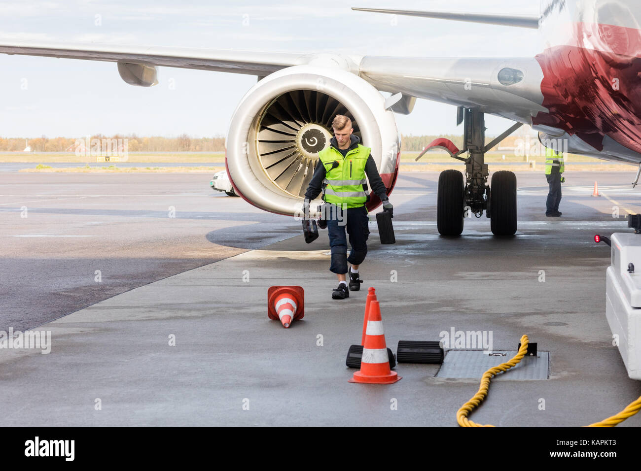 Worker Carrying Chocks By Airplane On Wet Runway Stock Photo