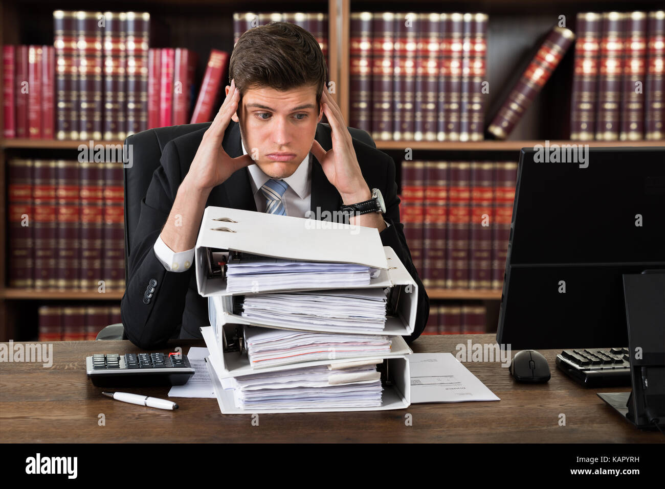 Stressed attorney looking at heap of binders at desk in office Stock