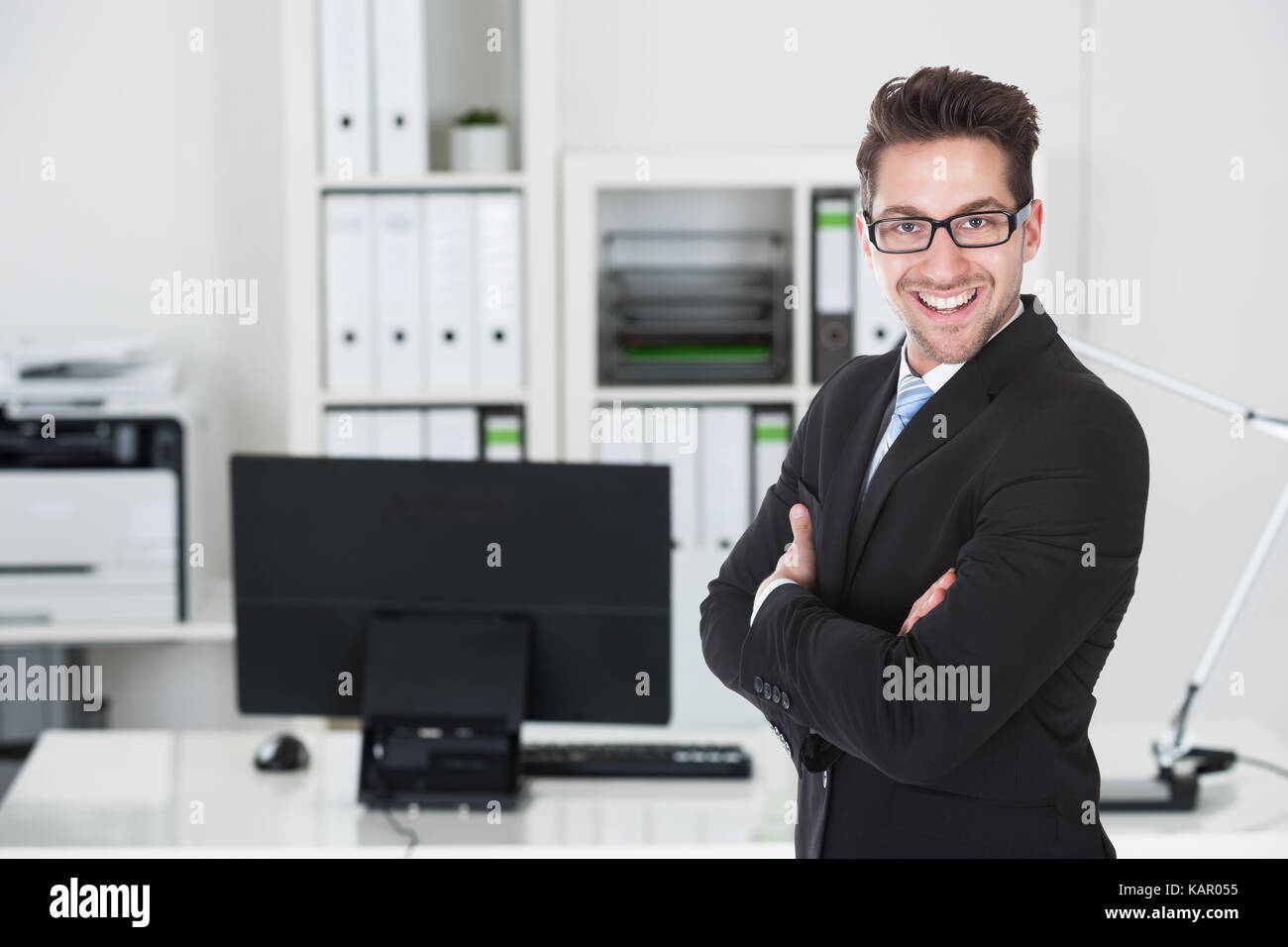 Portrait of confident young businessman standing arms crossed in office ...