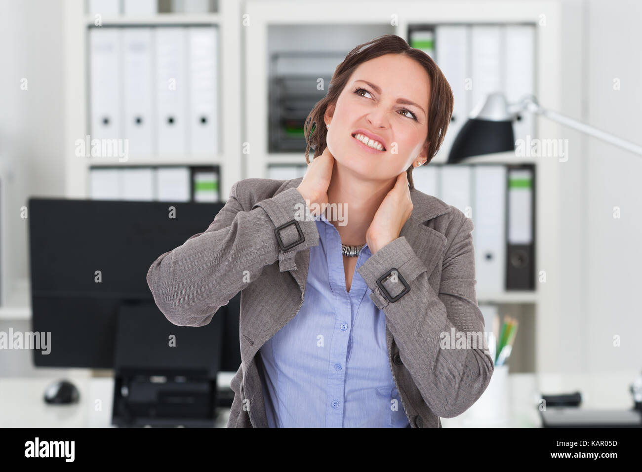 Young businesswoman suffering from neck pain in office Stock Photo - Alamy