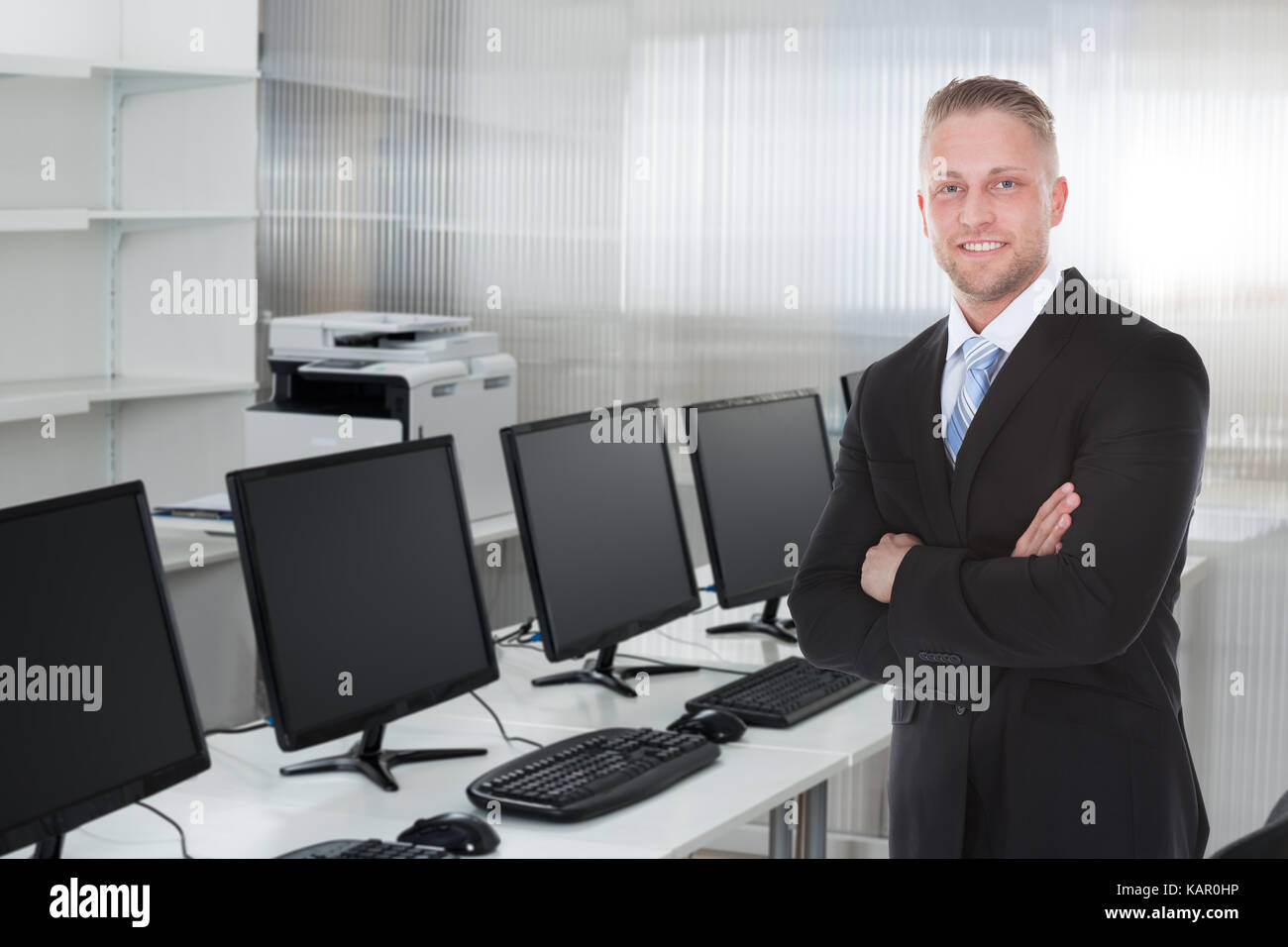 Portrait of young businessman standing arms crossed in office Stock ...