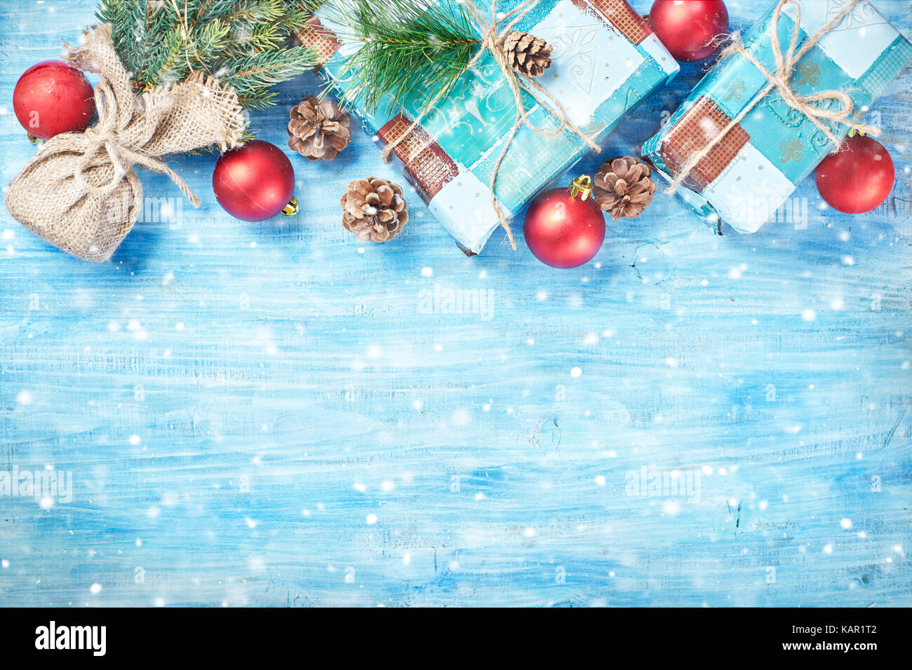 Top view of Christmas background on blue wooden board with fir, red decorations, snow and gift boxes forming top rim. Copy space. Stock Photo