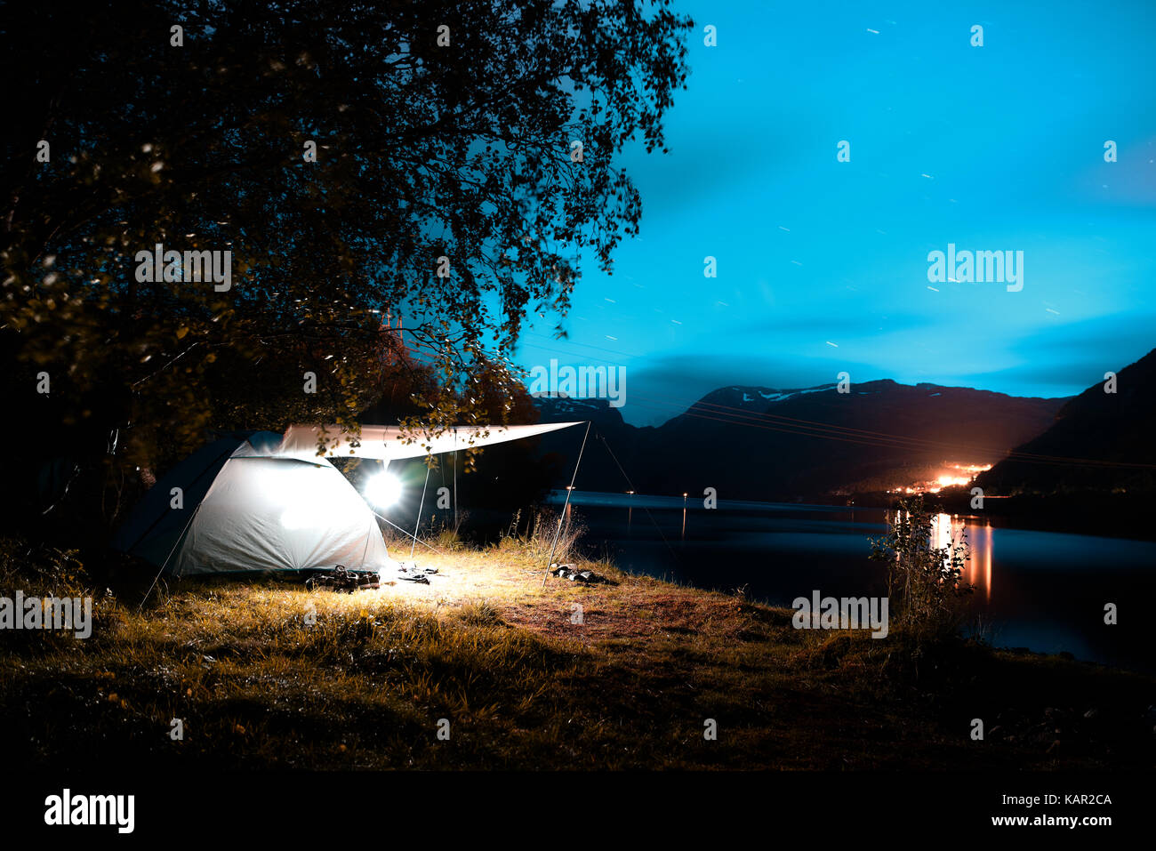Camping at the fjord at night with mountains, a city and a blue sky in the distance in Norway Stock Photo