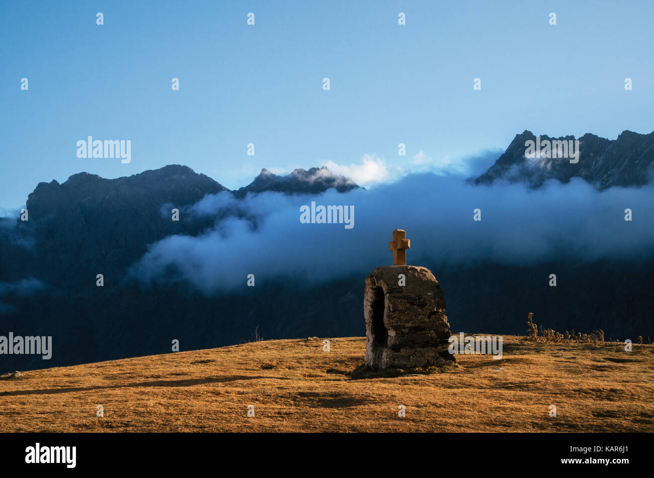 Christian Cross on stone on mountain among clouds. Morning time in autumn Stock Photo