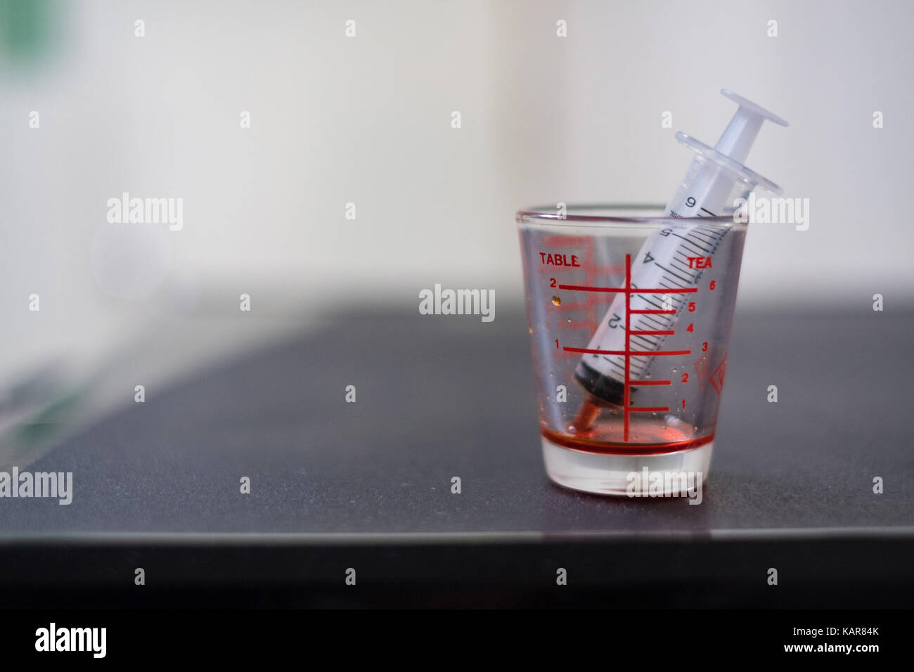 syringe with medicine syrup in a Pharmaceutical glass measuring cup for