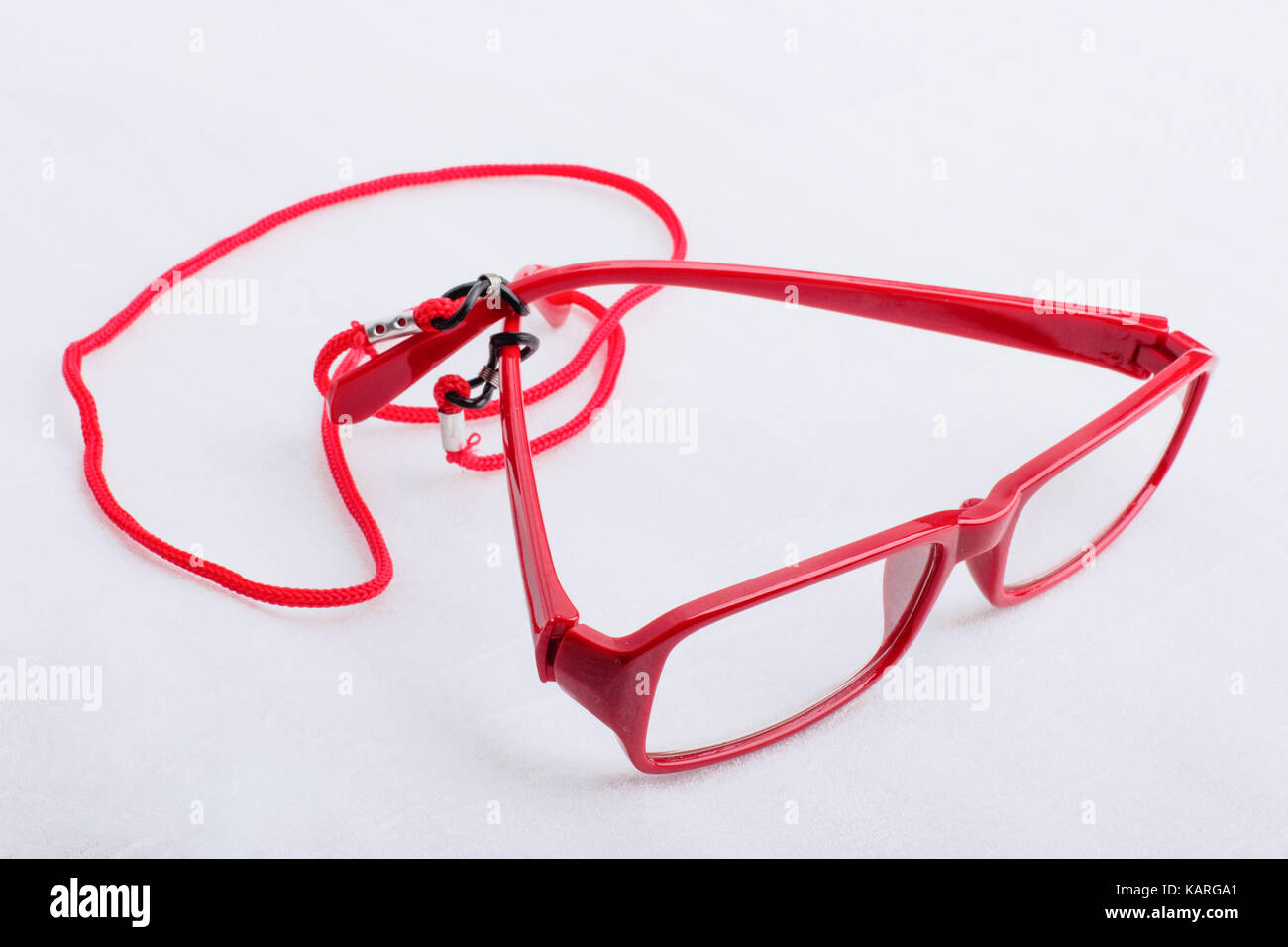 Red reading glasses with red neck strap attached to them, on a white surface. Stock Photo