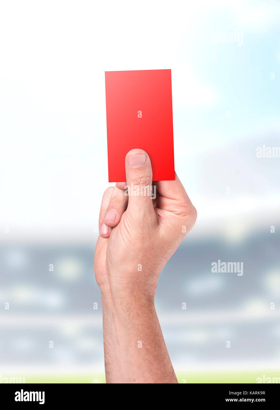 A male sports referee or umpire hand holding a red card up in the air on a sports stadium background in the day time Stock Photo
