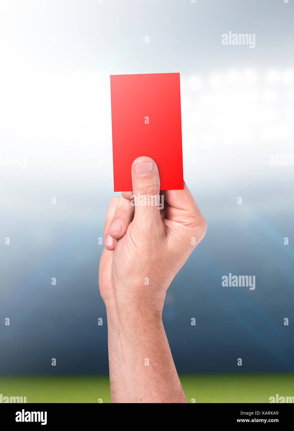 A male sports referee or umpire hand holding a red card up in the air on a sports stadium background in the night time Stock Photo