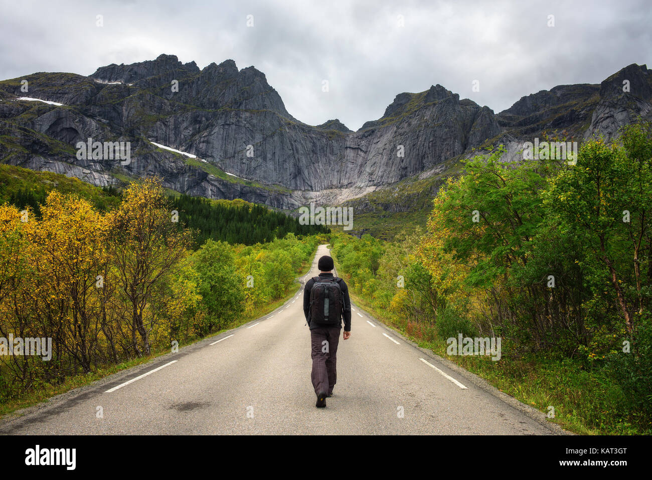Hiker carrying a backpack walks on a scenic road on Lofoten islands in Norway. Concept for loneliness and relaxation. Stock Photo