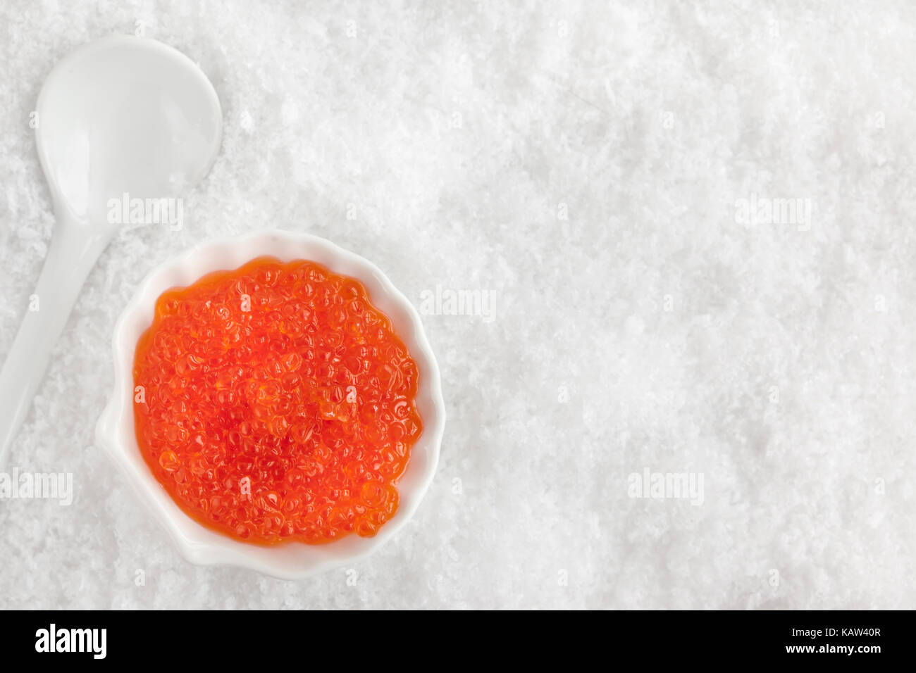 Delicious red caviar in bowl on white snow background, top view Stock Photo