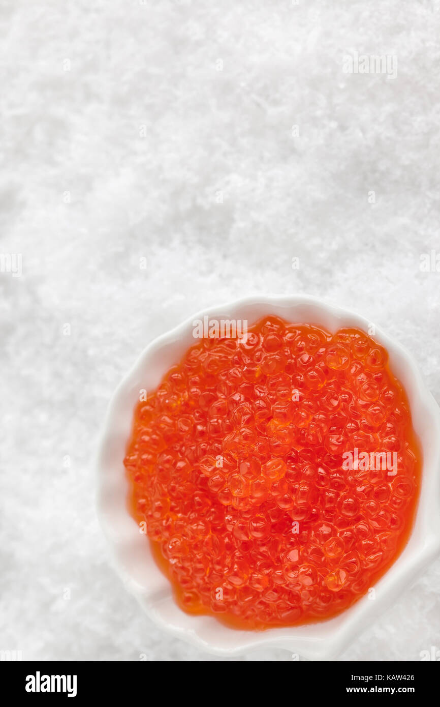 Delicious red caviar in bowl on white snow background, top view Stock Photo