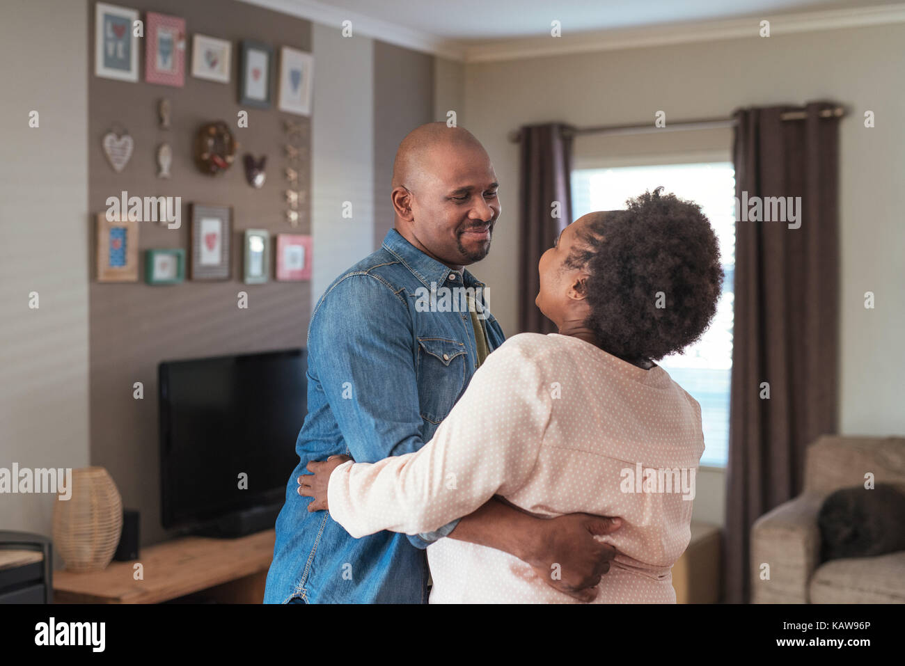 African couple smiling and dancing together in their living room Stock Photo