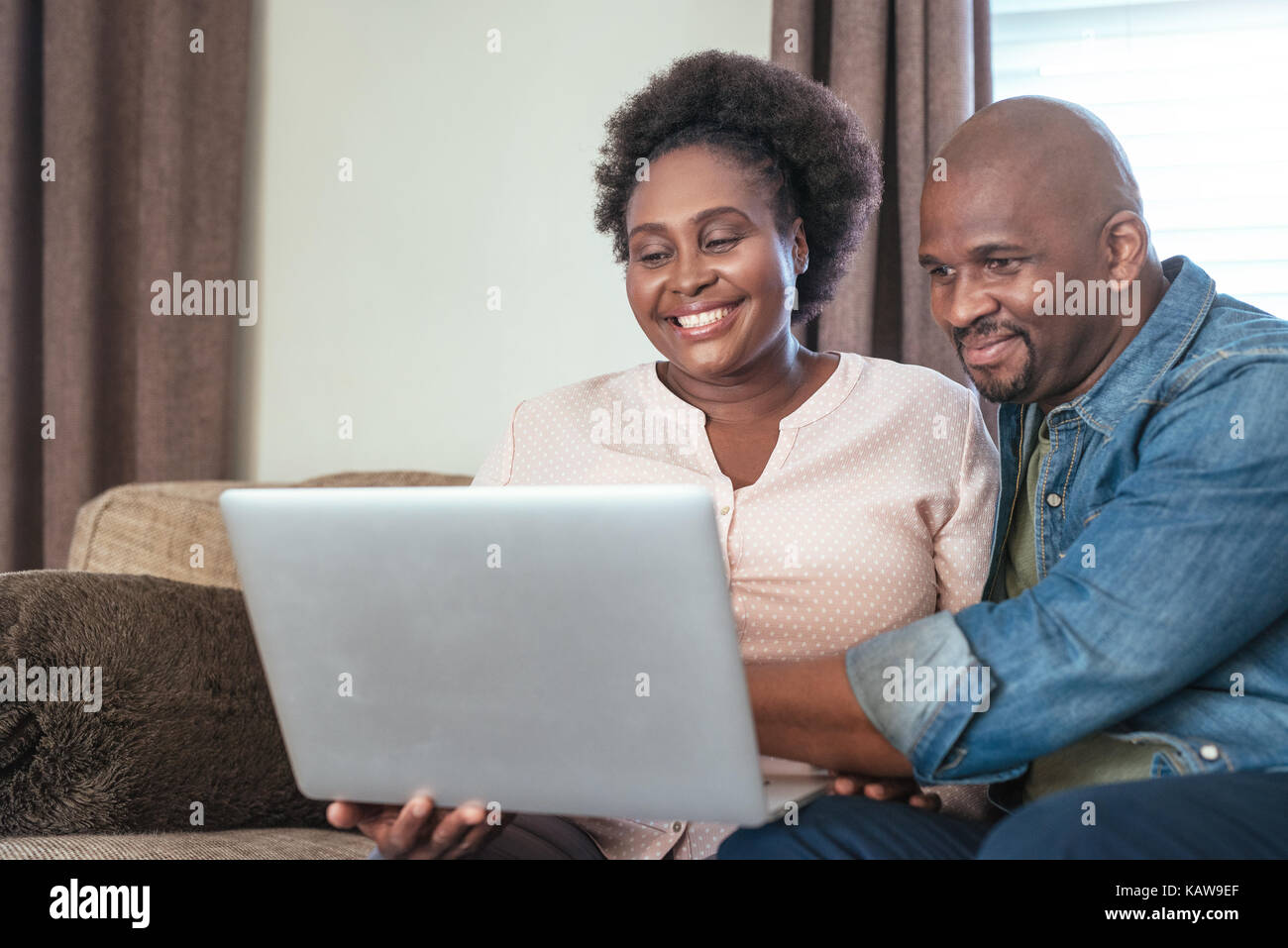 Laughing African couple sitting on a sofa using a laptop Stock Photo
