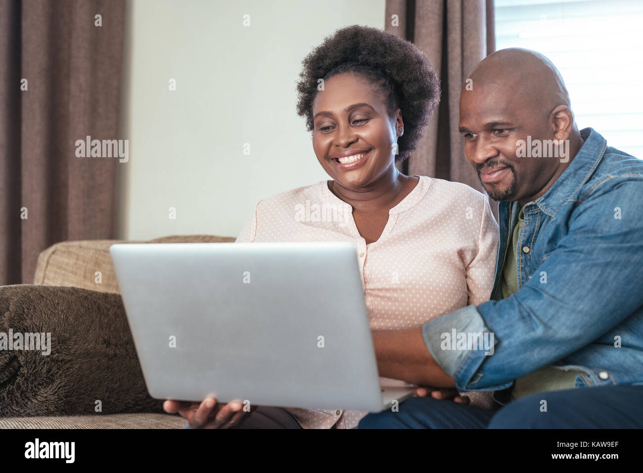 Laughing African couple sitting on a sofa using a laptop Stock Photo ...