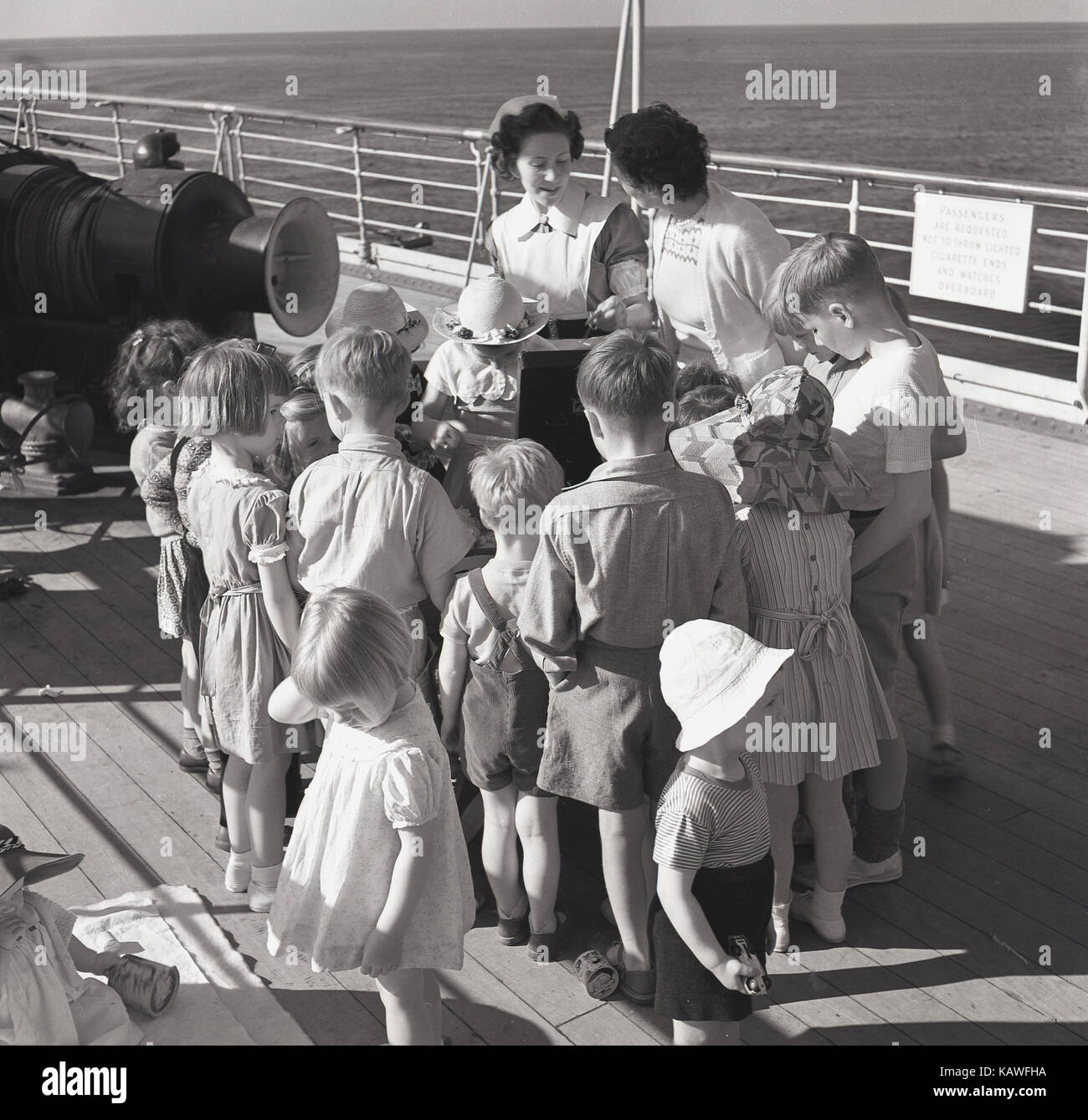1950s, historical, young children on board a Union-Castle steamship gather on the deck around a gramophone or record player to listen to some music, supervised by a ship's nurse. Stock Photo