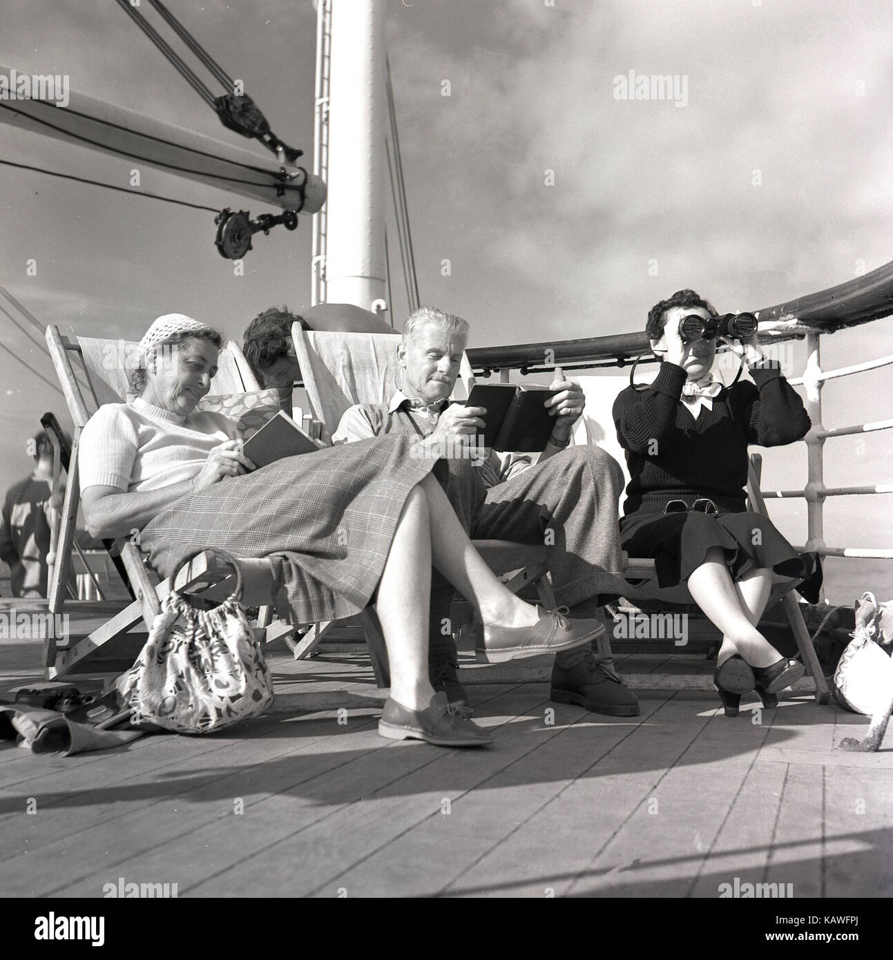 1950s, historical, three passengers on the Union-Castle liner, traveling from Southhampton to Cape Town, relax on the deck, two of them reading and a lady looking through a pair of binoculars. Stock Photo