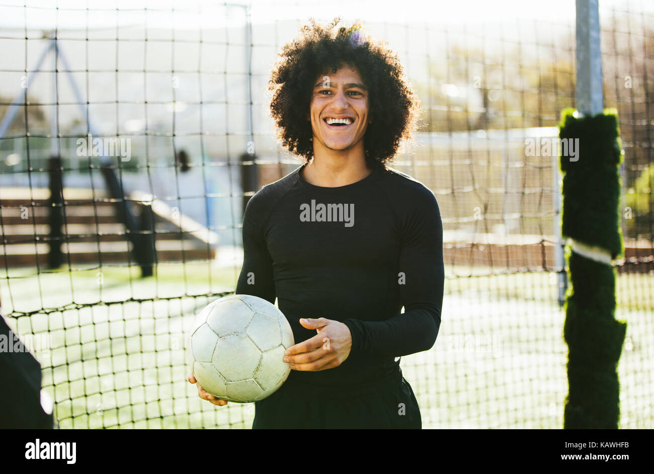 Portrait of teenage football player holding a ball in his hand and laughing. Young man training on soccer field. Stock Photo