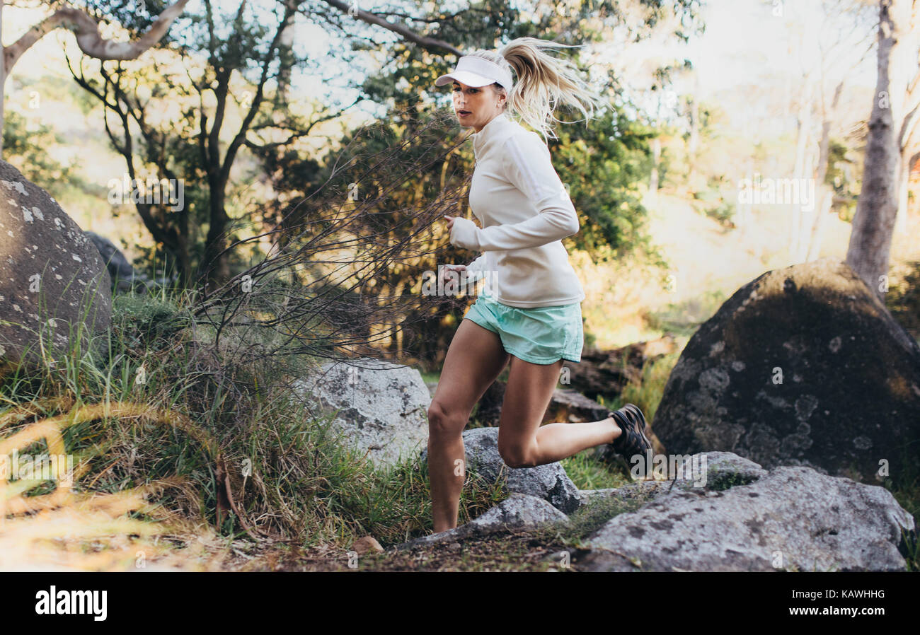 Morning runner jogging in a park. Woman running through rocks and bushes. Stock Photo
