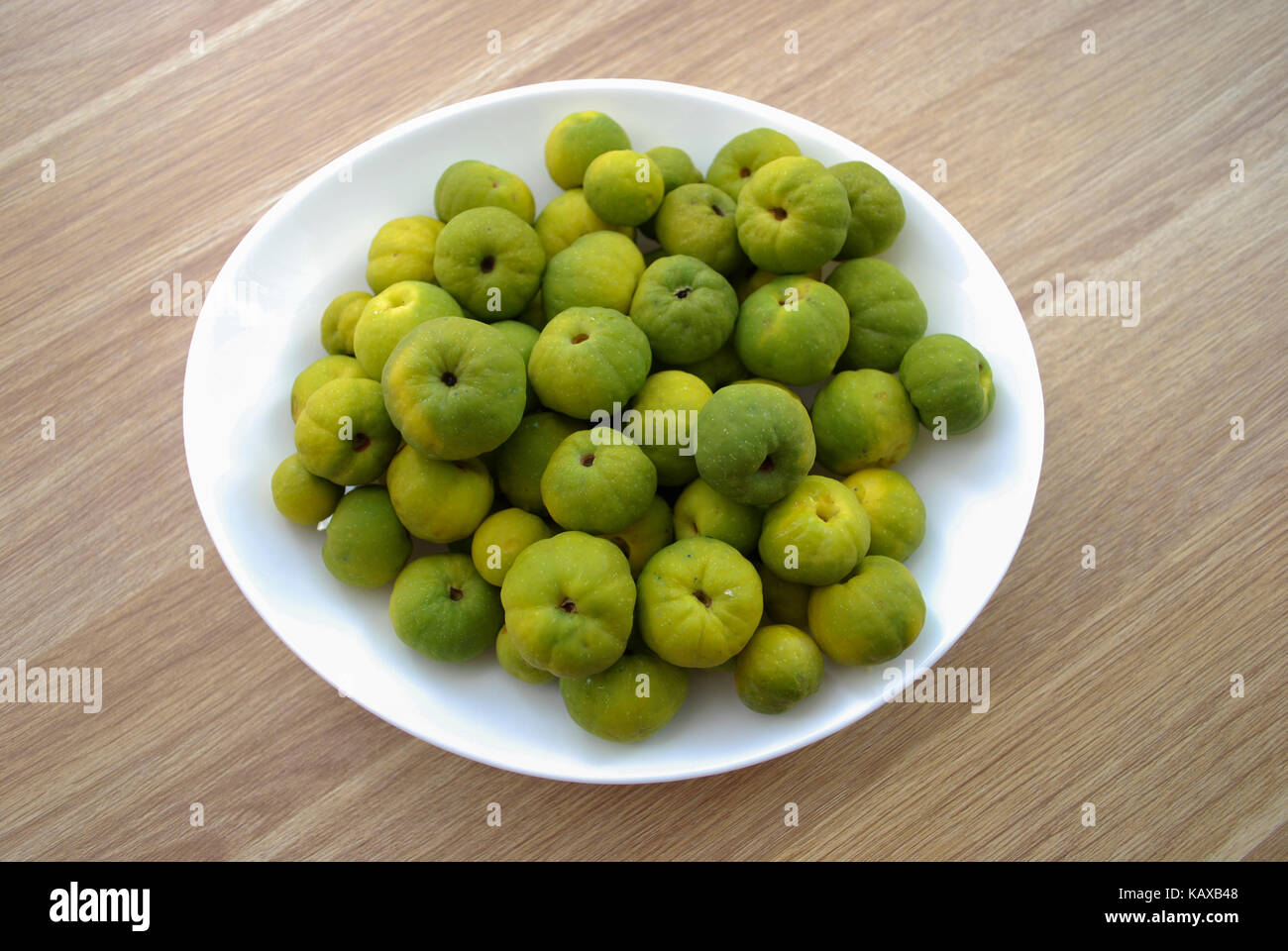 Chaenomeles japonica (known as Maule's quince) green and yellow fruits on the white plate. Wooden background. Stock Photo