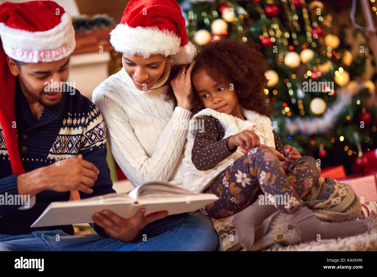 Afro American family with daughter look at book bought for Christmas Stock Photo