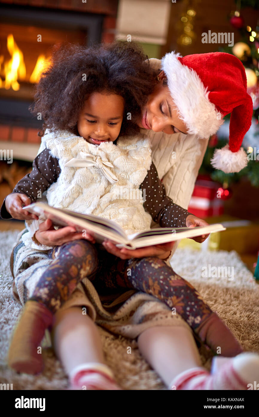 Pretty Afro American child with mother reading book for Christmas Stock Photo