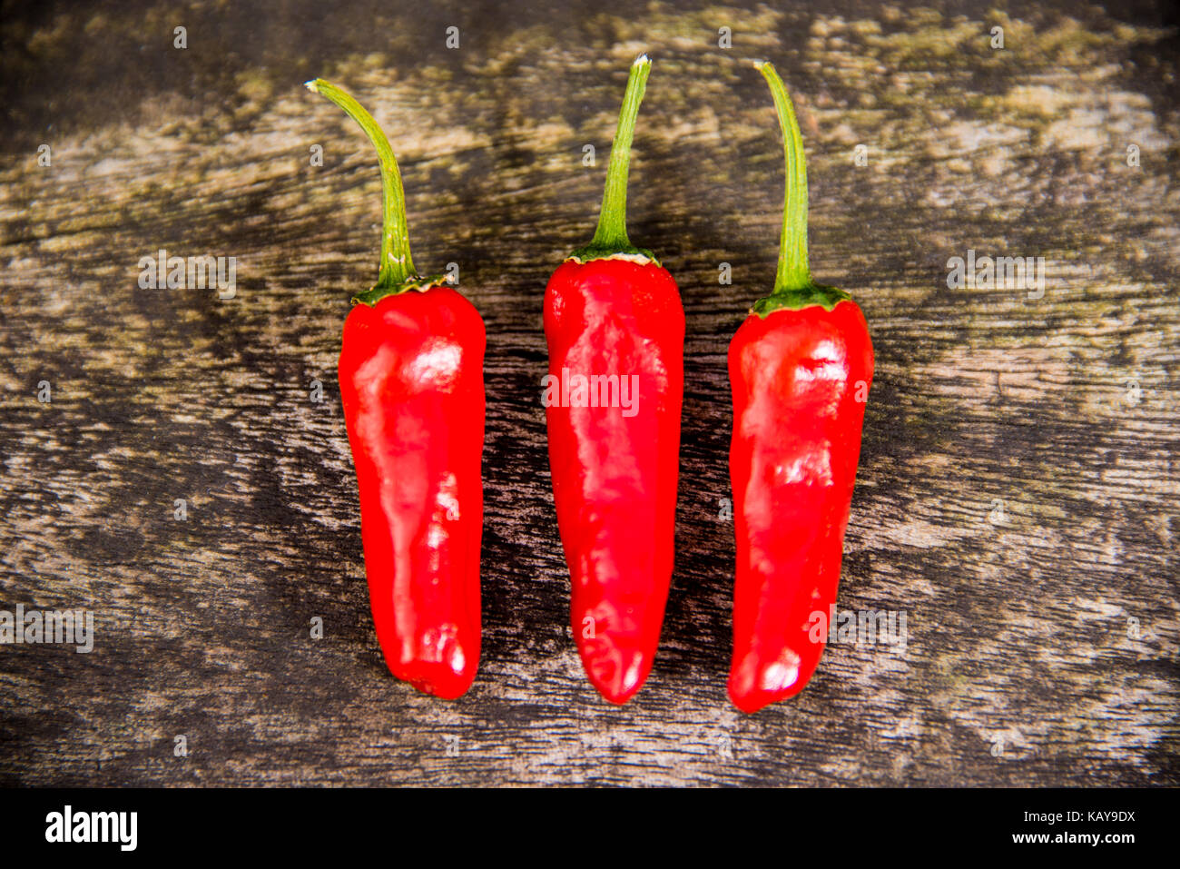 Three Red Chilli Peppers on a Wooden Background Stock Photo - Alamy