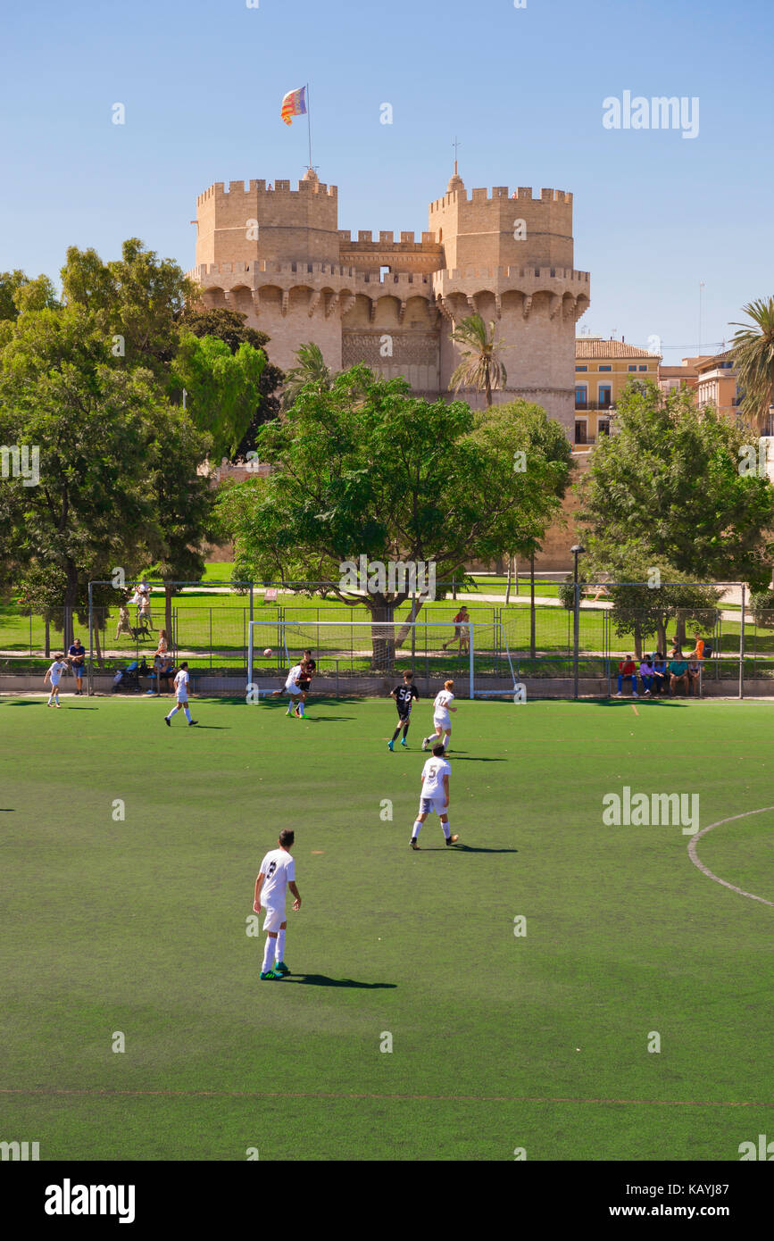 Valencia Rio Turia garden, overlooked by the Torres Serranos city gate, teenagers play a football match on a pitch in the Turia riverbed garden, Spain Stock Photo