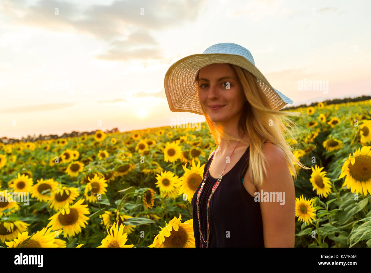 Woman with hat on sunflowers field at sunset Stock Photo