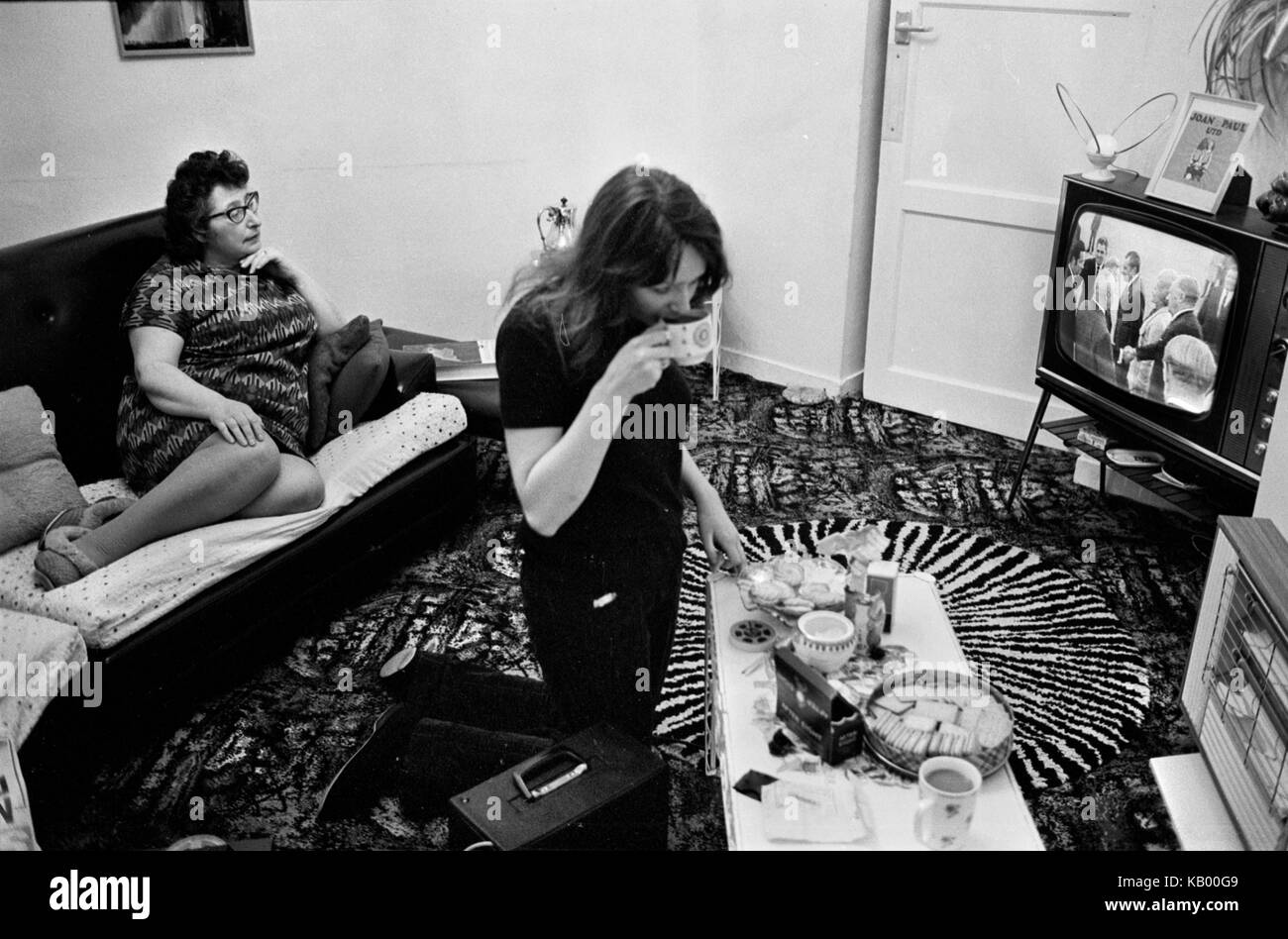 Family at home 1970s in living room interior watching TV television.  They are watching the BBC television news Presidents Nixon and his wife Pat Nixon are meeting and greeting. Note the butterfly television aerial on the top of the TV set. The home made card reads 'Joan Paul UTD.' After Eight chocolates and a plate and tin biscuits. HOMER SYKES Stock Photo