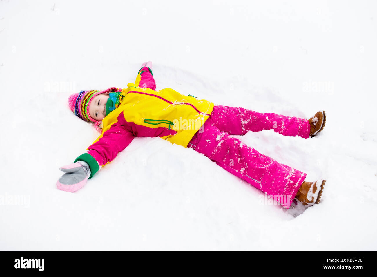 Child making snow angel. Kids play in winter snowy park. Family