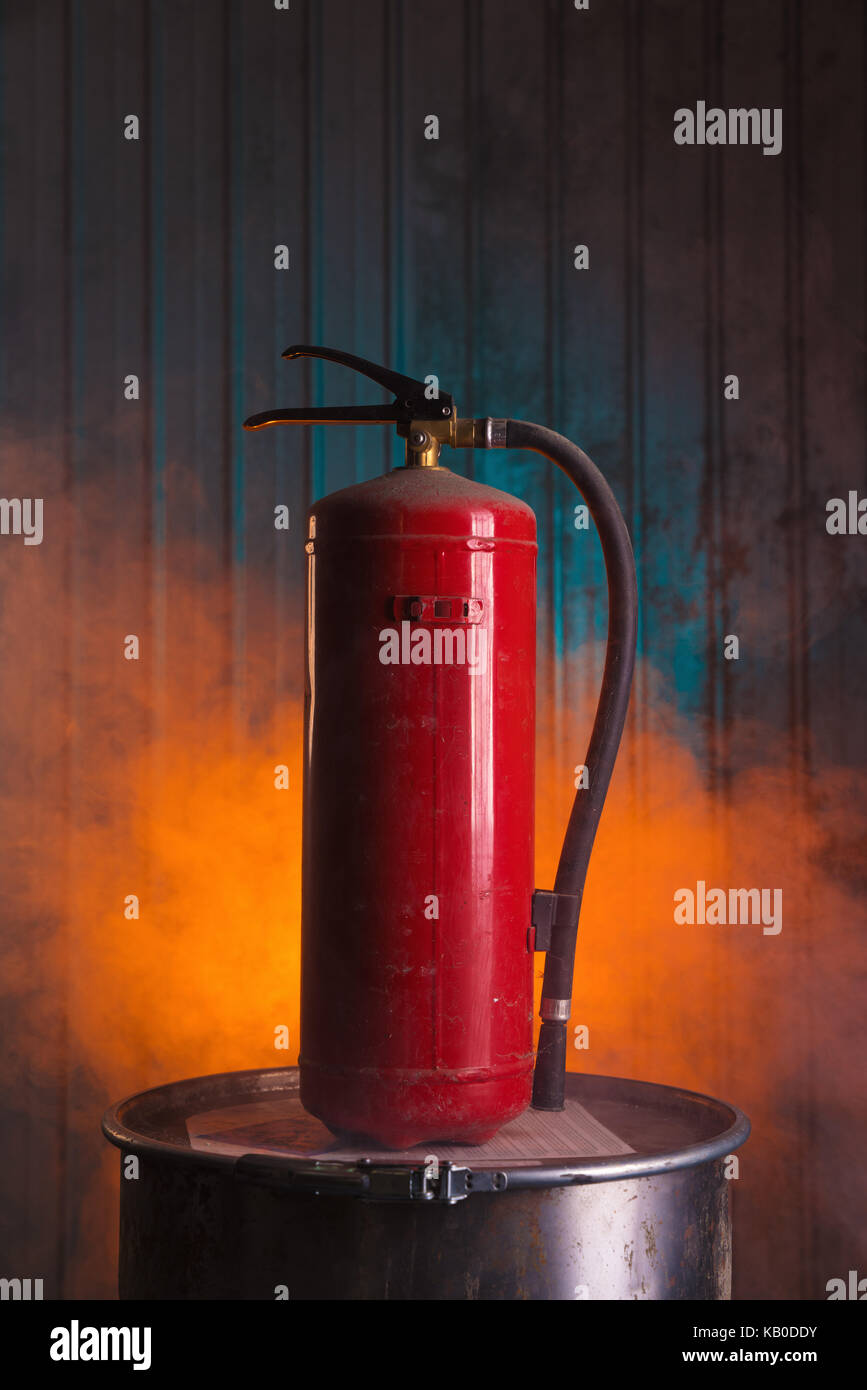 Red fire extinguisher on urban style background with orange smoke Stock Photo