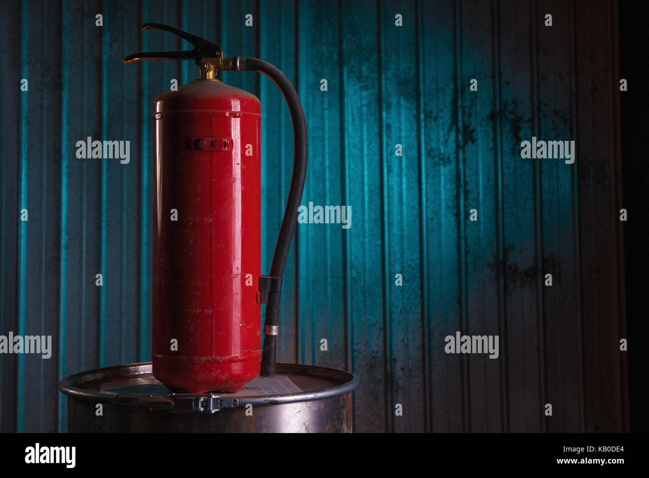 Red fire extinguisher on blue colored metal background Stock Photo