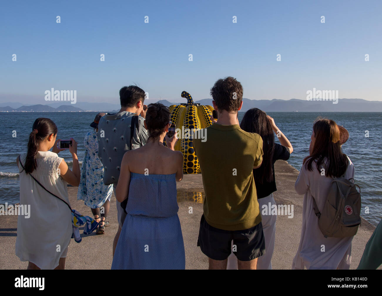 Tourists taking pictures of the yellow pumpkin by yayoi kusama on pier at sea, Seto Inland Sea, Naoshima, Japan Stock Photo