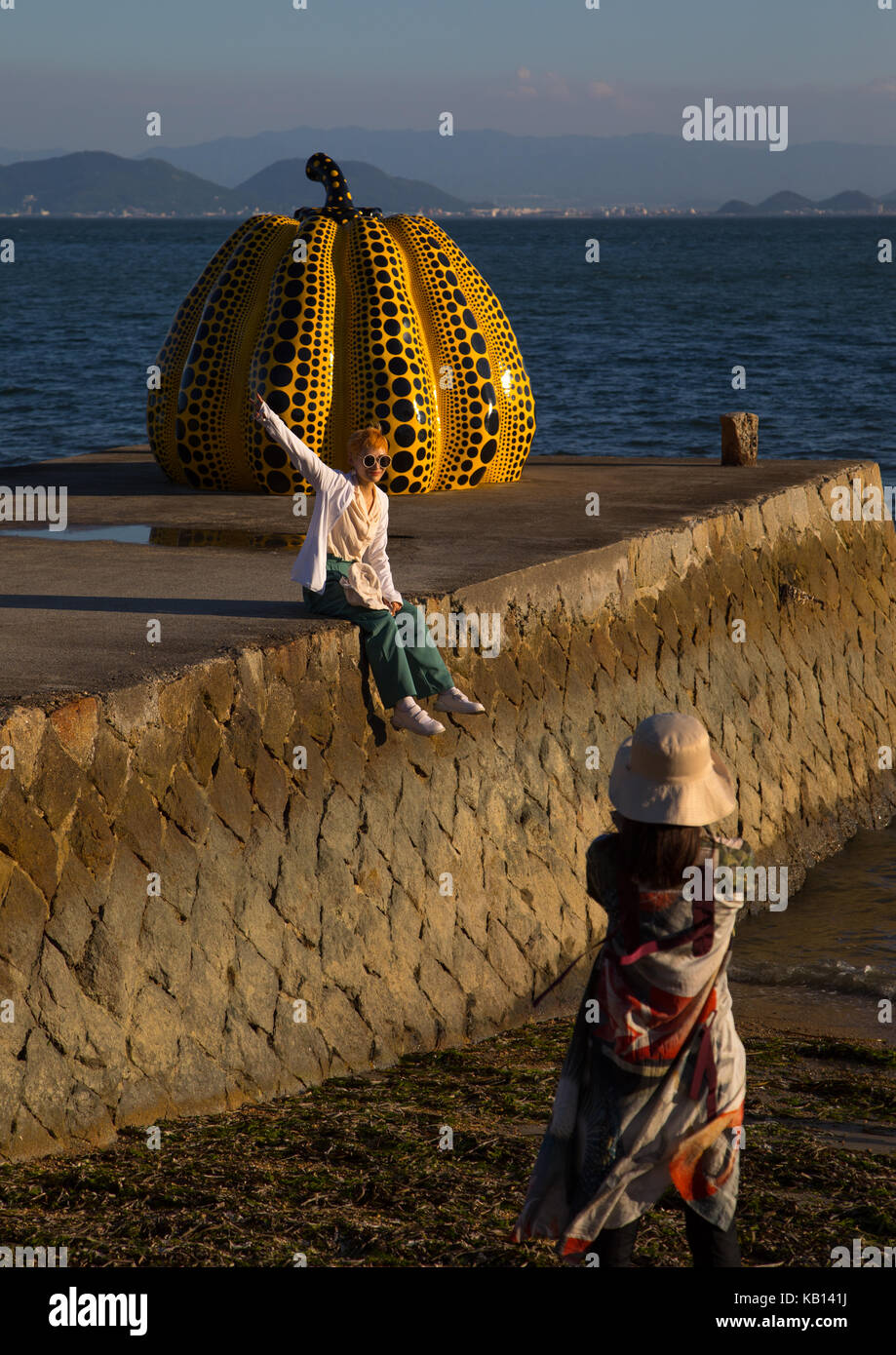 Tourist taking pictures of the yellow pumpkin by yayoi kusama on pier at sea, Seto Inland Sea, Naoshima, Japan Stock Photo