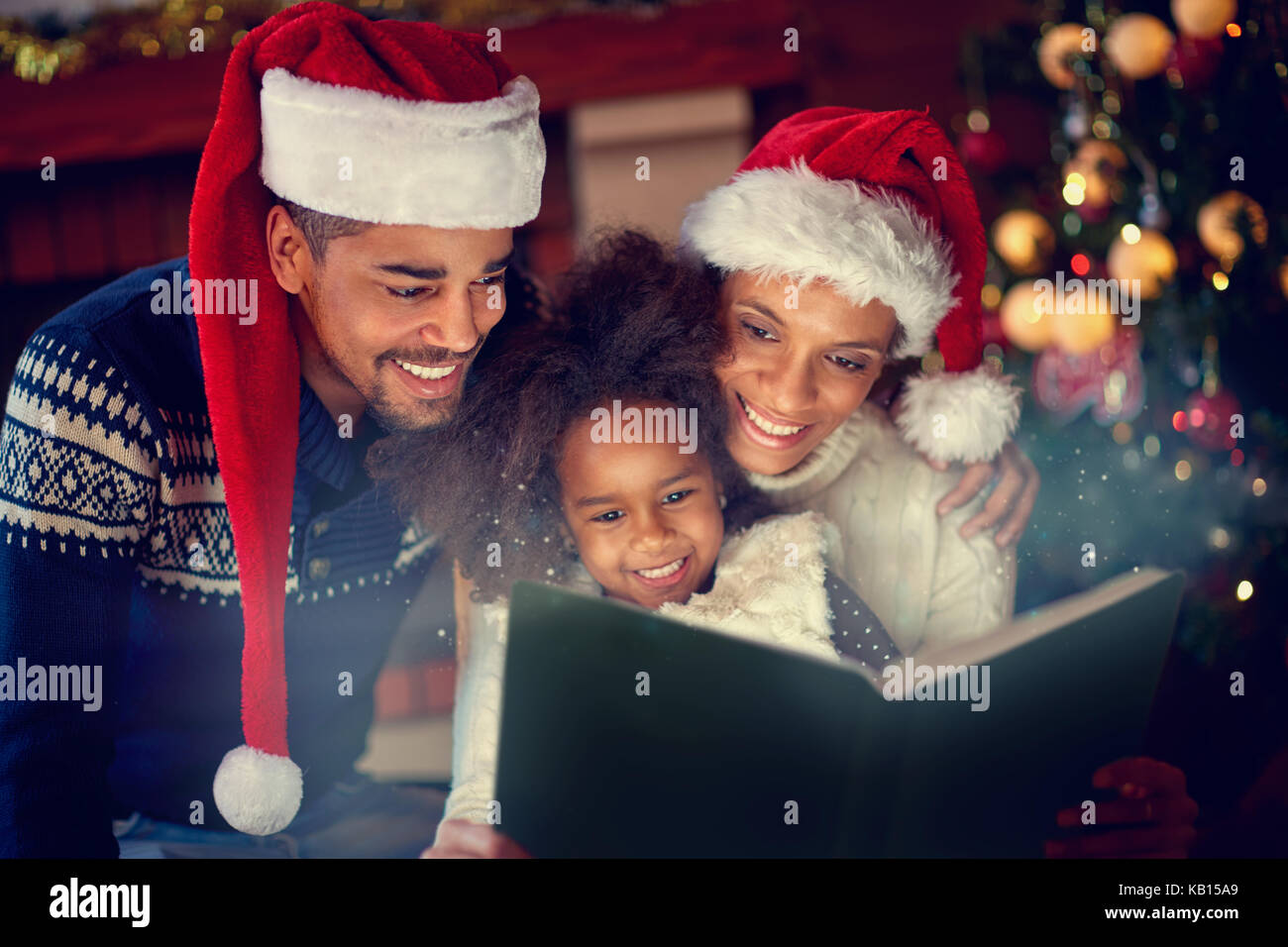 Young afro American parent together reading their little daughter Christmas fairytales Stock Photo