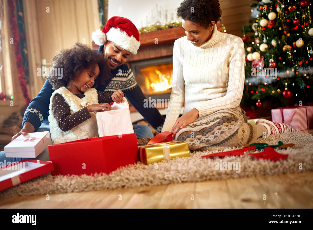 afro American parents looking in their little girl which opens Christmas presents Stock Photo